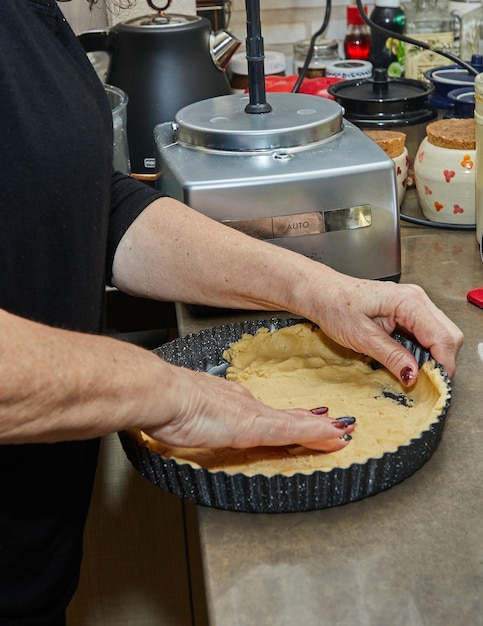 Cook kneads the dough in a mold for making a pie in the kitchen