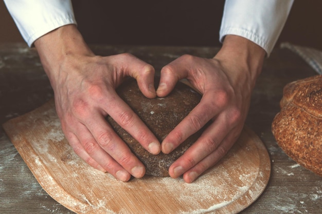 Cook men holding hand in the form of heart on the top of kneaded dough