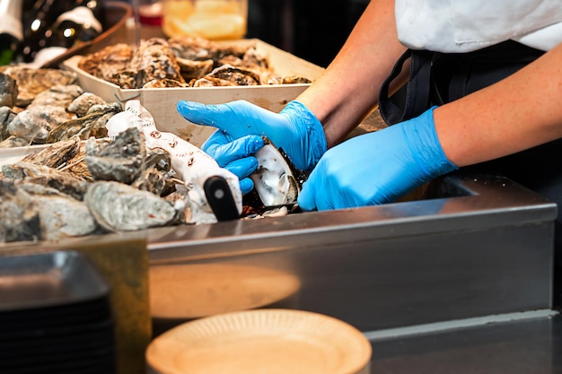 A cook opening an oyster shell in a fast food restaurant cooking seafood in a cafe