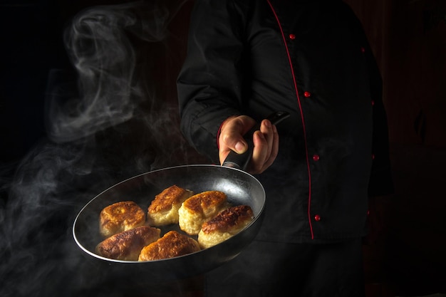 The cook prepares donuts in a frying pan The concept of preparing a Ukrainian national dish in the kitchen of a restaurant or hotel Black space for advertising