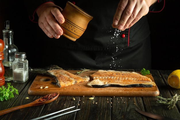 The cook prepares fresh salmon fish trout smorgus sprinkling the ingredients with salt