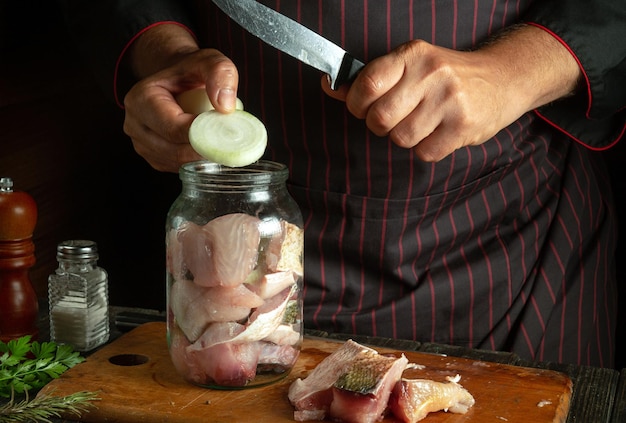 The cook prepares herring in the kitchen from fish steaks and aromatic spices Canning fish in a jar with salt and onions