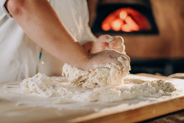 The cook prepares the pizza dough. Cooking. A man kneads the dough with his hands for making pizza in the oven.