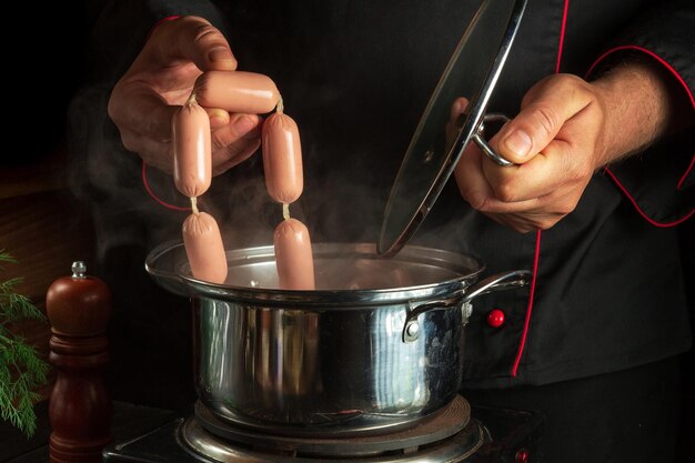 Cook puts Vienna sausage in a saucepan Working environment in the kitchen of a restaurant or cafe Preparing breakfast or dinner