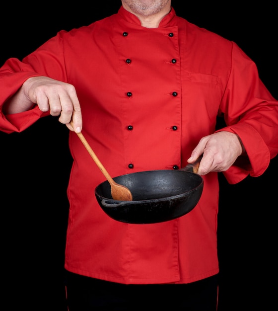 Cook in red uniform holding an empty  black frying pan and wooden spoon