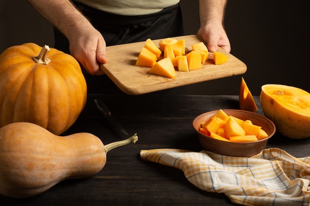 Cook throws slices of pumpkin from a cutting board into a deep bowl. 