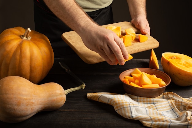 Cook throws slices of pumpkin from a cutting board into a deep bowl. 