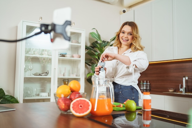 Cook with pleasure. Cheerful curly haired girl keeping smile on her face while looking at her gadget