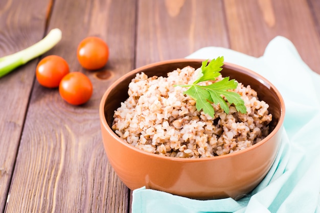 Cooked buckwheat in a bowl with a leaf of parsley and cherry tomatoes on a wood table