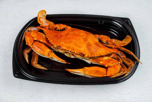 Cooked crab on black plastic plate on gray background