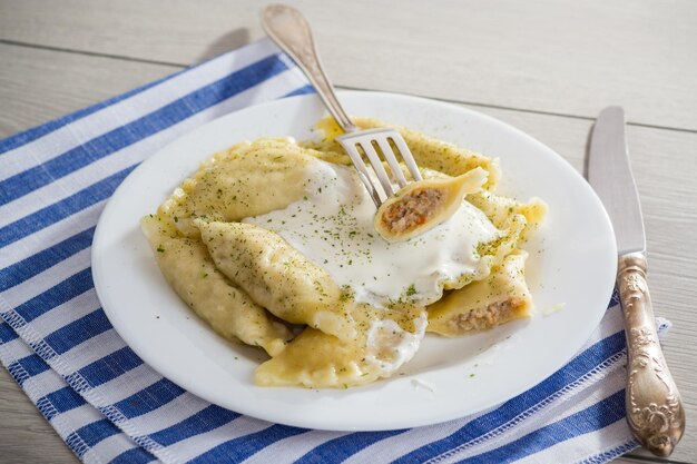 cooked dumplings with meat spices and sour cream in a plate on a light wooden table