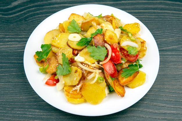 Cooked fried potatoes with herbs and vegetables in a white plate on a wooden table