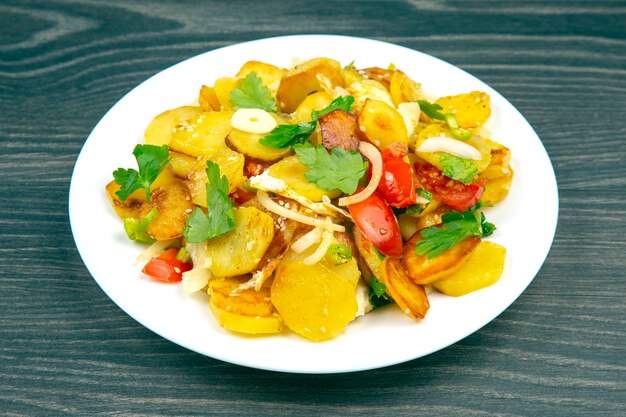 Cooked fried potatoes with herbs and vegetables in a white plate on a wooden table