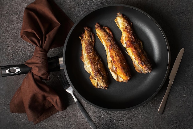 Cooked fried white fish in a pan, close-up on a dark background