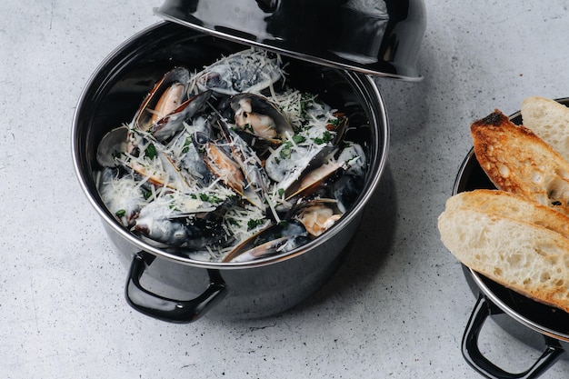 Cooked oysters in a pot sprinkled with parmesan and greens On a table