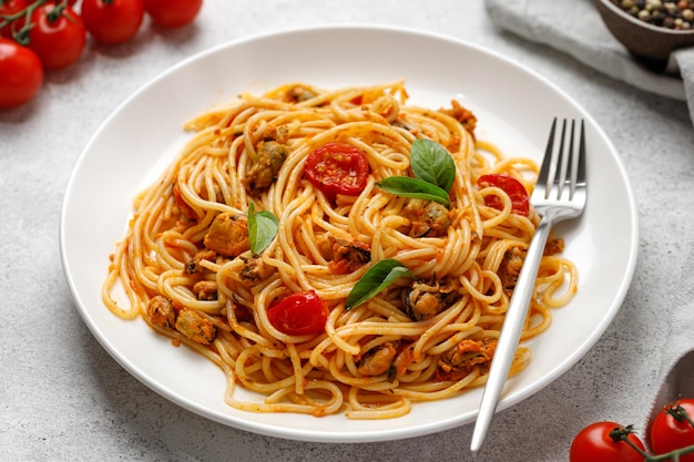 Cooked pasta with mussels cherry tomatoes basil in white plate with fork Close up Mediterranean food