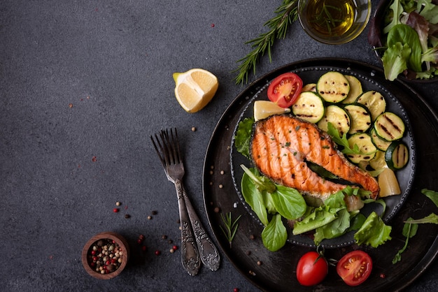 Cooked salmon fish with vegetables on dark background