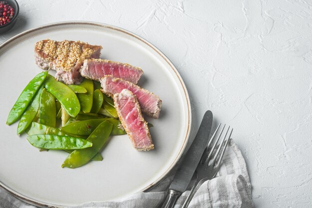 Photo cooked tuna steak in sesame set with spring onions and sugar snap peas, on plate, on white stone