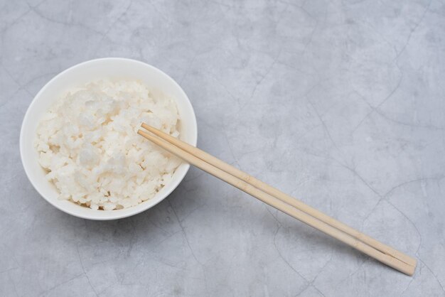 Cooked white rice in white bowl with wood sticks on grey background Selective focus Asian food concept