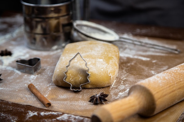 A cookie cutter in the form of a christmas tree is leaning on the dough cinnamon and cloves are lyin...