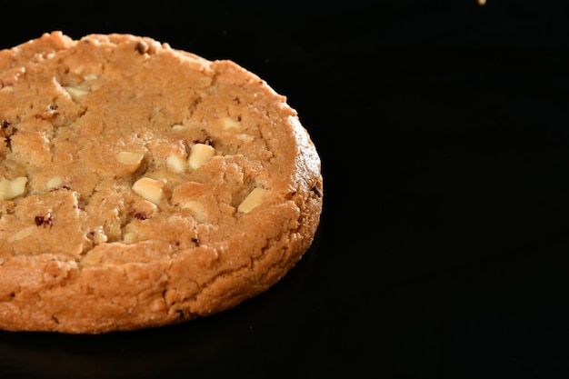 A cookie with white macadamia nuts sits on a black surface.