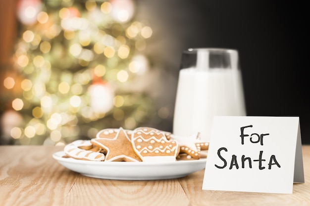 Cookies milk and a note for Santa on the table against the background of the Christmas tree