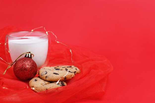 Photo cookies with chocolate chips, a glass of milk and a christmas tree red toy on a new year's background