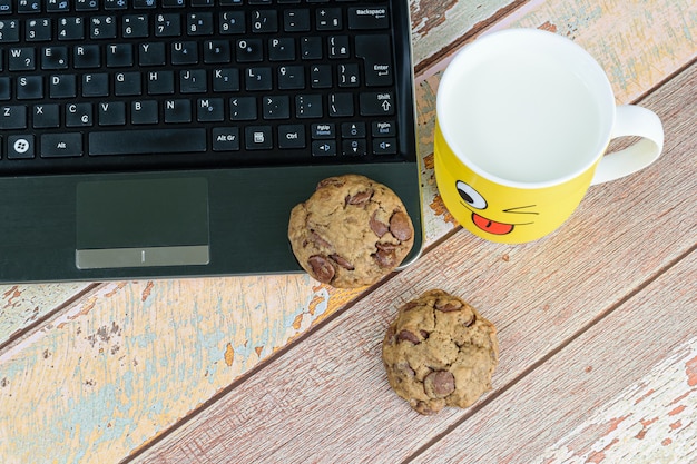 Photo cookies with drops of chocolate on the laptop, next to a yellow mug with milk, break for e-learning.