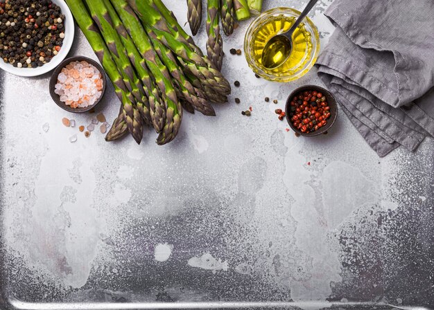 Cooking asparagus background. Bunch of fresh green organic asparagus ready for cooking on baking tray with olive oil and seasonings, good for healthy dieting, top view, close up, space for text