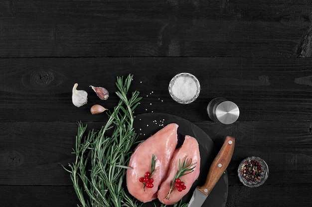 Cooking chicken breasts On the table are spices rosemary red and black pepper Concept healthy food On a black wooden background Top view with copy space Still life Flat lay