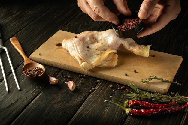 Cooking a chicken leg on a cutting board before grilling The chef adds aromatic spices to the chicken thigh for flavor