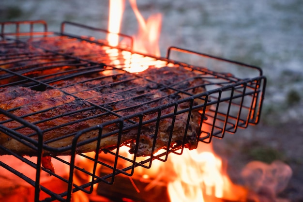 Cooking chicken meat over charcoal Chicken meat fried with a crust on a wire rack during grill cooking Backlight from a burning fire and smoke in the late evening