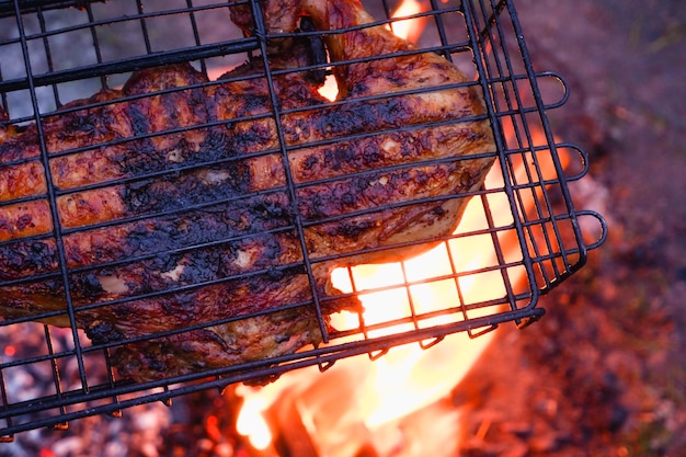 Cooking chicken meat over charcoal Chicken meat fried with a crust on a wire rack during grill cooking Backlight from a burning fire and smoke in the late evening