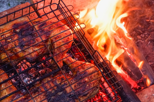 Cooking chicken meat over charcoal Chicken meat fried with a crust on a wire rack during grill cooking Backlight from a burning fire and smoke in the late evening