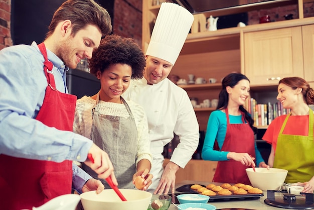 cooking class, culinary, bakery, food and people concept - happy group of friends and male chef cook baking in kitchen