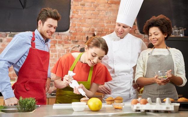 cooking class, culinary, bakery, food and people concept - happy group of friends and male chef cook baking in kitchen