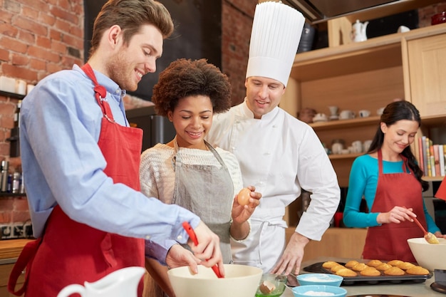 cooking class, culinary, bakery, food and people concept - happy group of friends and male chef cook baking in kitchen