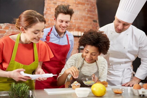 cooking class, culinary, bakery, food and people concept - happy group of friends and male chef cook baking in kitchen