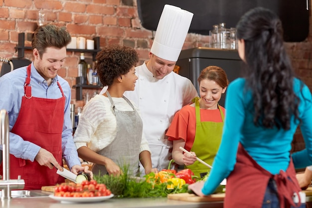 cooking class, culinary, food and people concept - happy group of friends and male chef cook cooking in kitchen