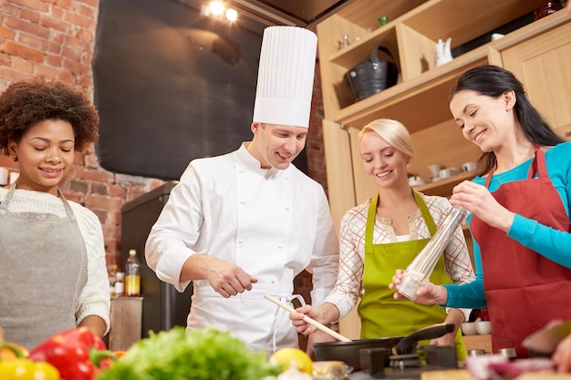 cooking class, culinary, food and people concept - happy group of women and male chef cook cooking in kitchen