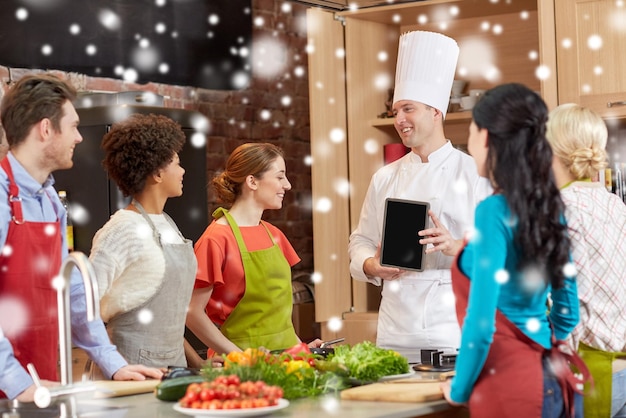 cooking class, culinary, food, technology and people concept - happy friends with chef cook showing blank tablet pc screen in kitchen over snow effect