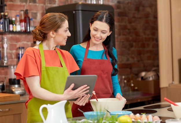 cooking class, friendship, food, technology and people concept - happy women with tablet pc computer in kitchen