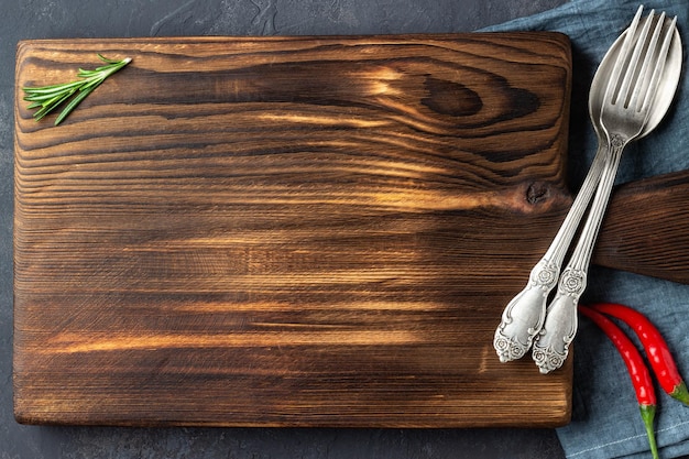 Cooking concept Vintage cutting board with spices and cutlery on dark stone background Copy space