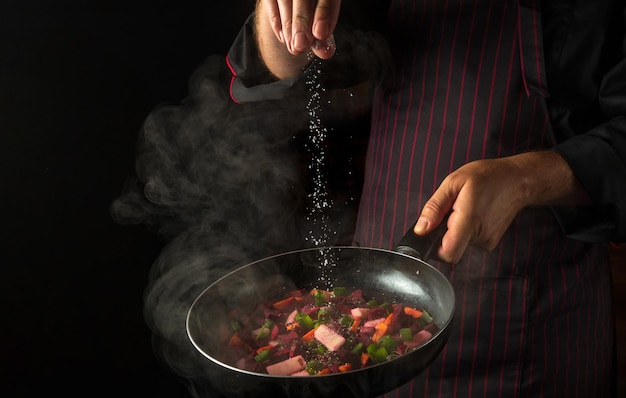 Cooking fresh vegetables The chef adds salt to a steaming hot pan Grande cuisine