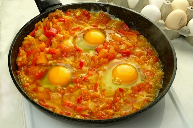 Cooking fried eggs shakshuka in vegetables sauce in frying pan. Jewish and arabic cuisine.