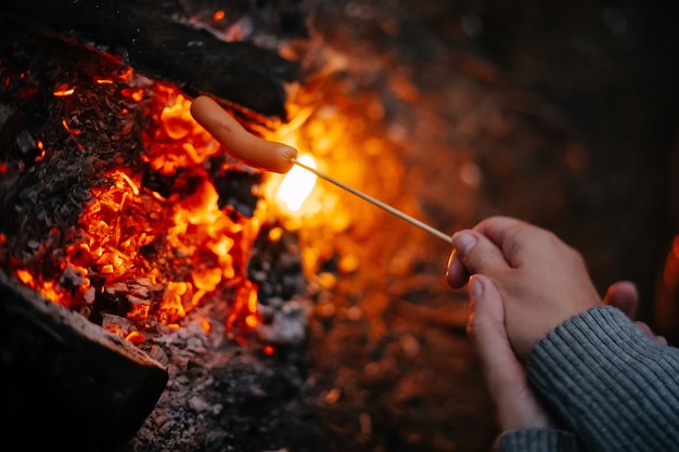 Cooking fried sausages on a fire on a wooden rod in a summer forest concept of tourism and camping