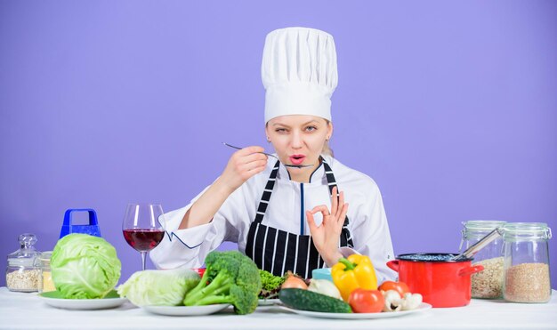 Photo cooking healthy food fresh vegetables ingredients for cooking meal professional cooking tips woman chef try taste food gourmet main dish recipes delicious recipe concept girl in hat and apron