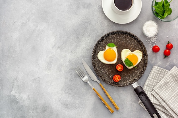 Cooking heart-shaped fried eggs in a pan with tomatoes and greens