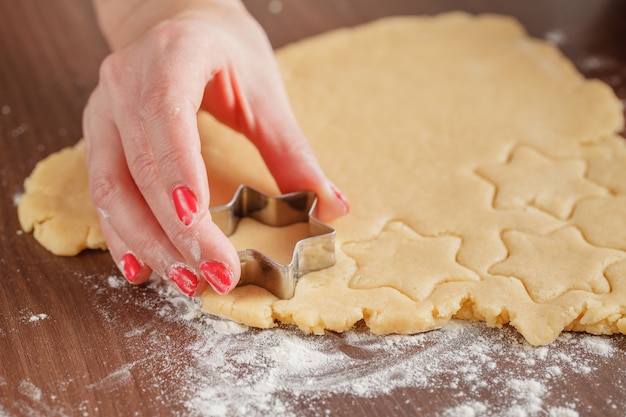 Cooking and home concept - close up of female hands making cookies from fresh dough at home