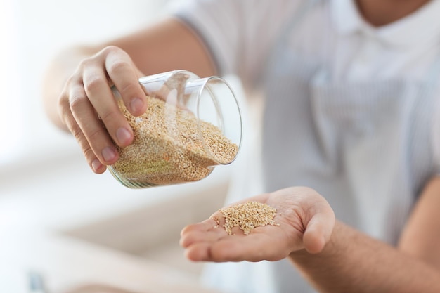 cooking and home concept - close up of male emptying jar with quinoa